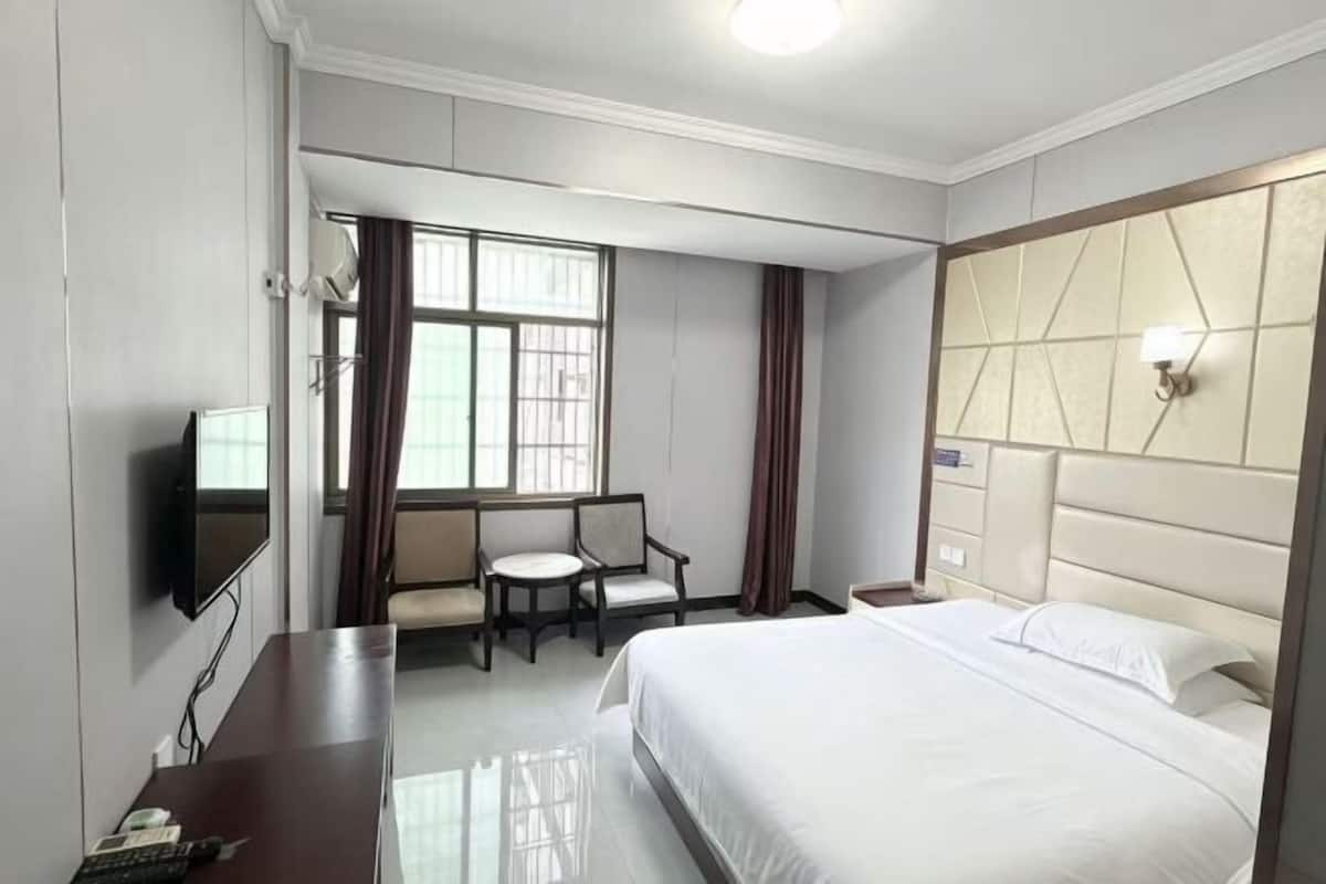 Una habitación de hotel con cama, escritorio, silla, televisor y ventana con cortinas.