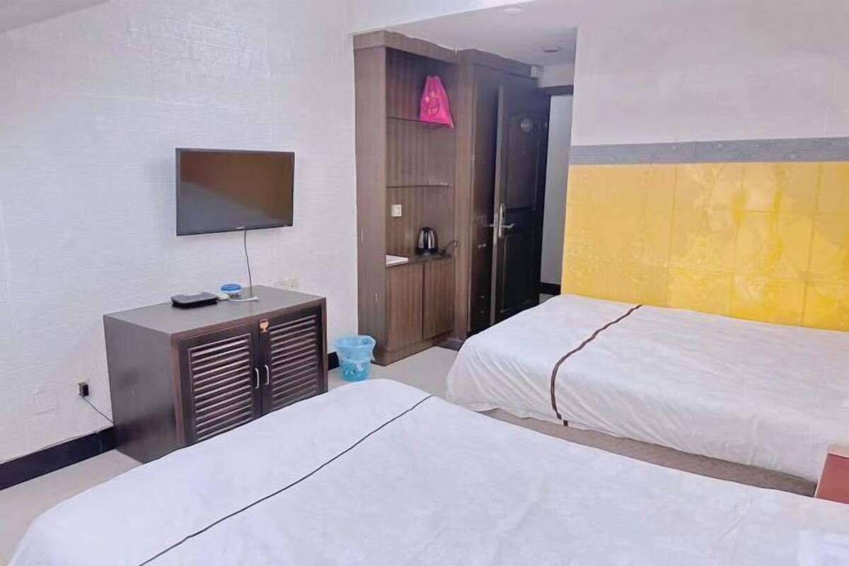 Habitación de hotel con dos camas, un televisor en la pared, un armario y una mesita con una tetera.