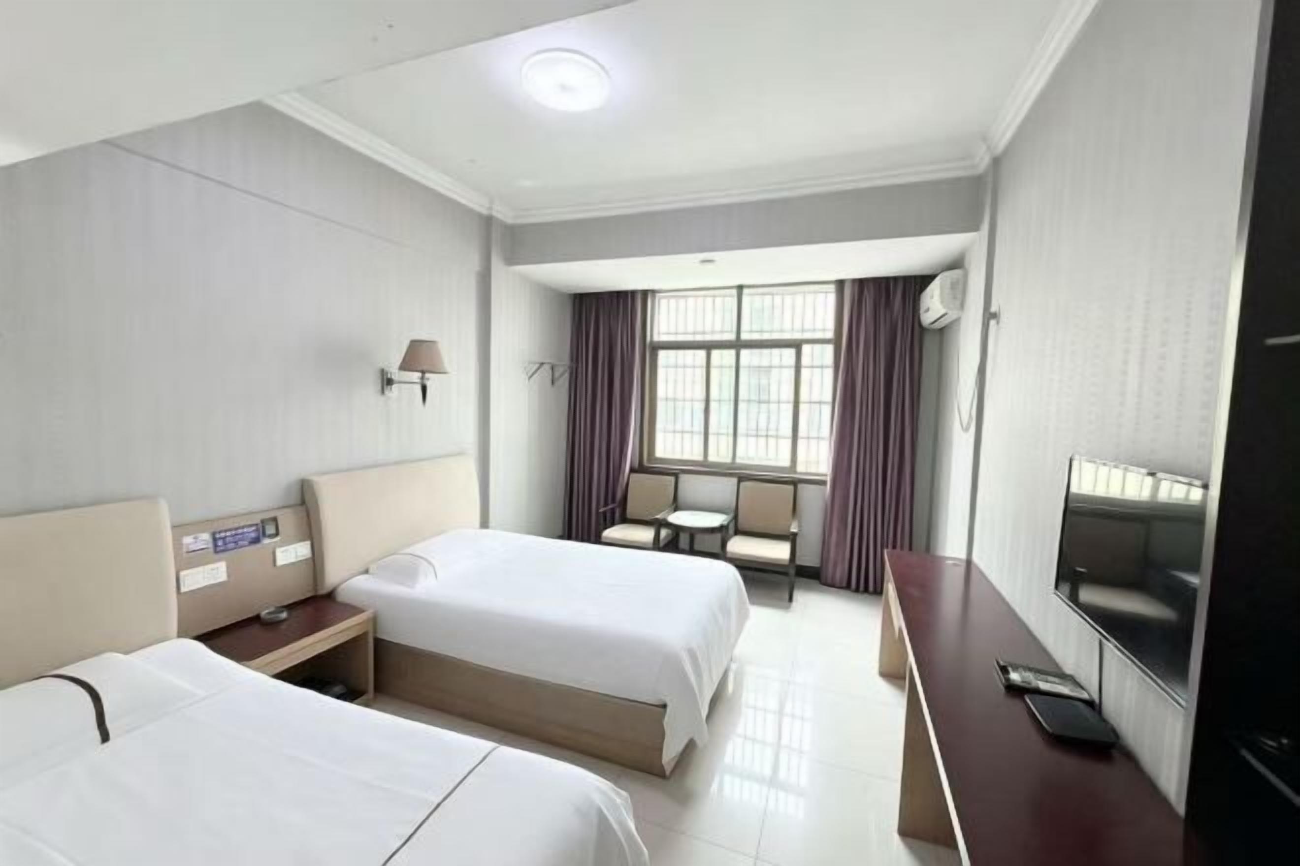 A hotel room with two beds, a desk, a TV, and a window with curtains.