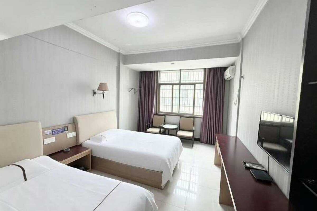Una habitación de hotel con dos camas, un escritorio, un televisor y una ventana con cortinas.