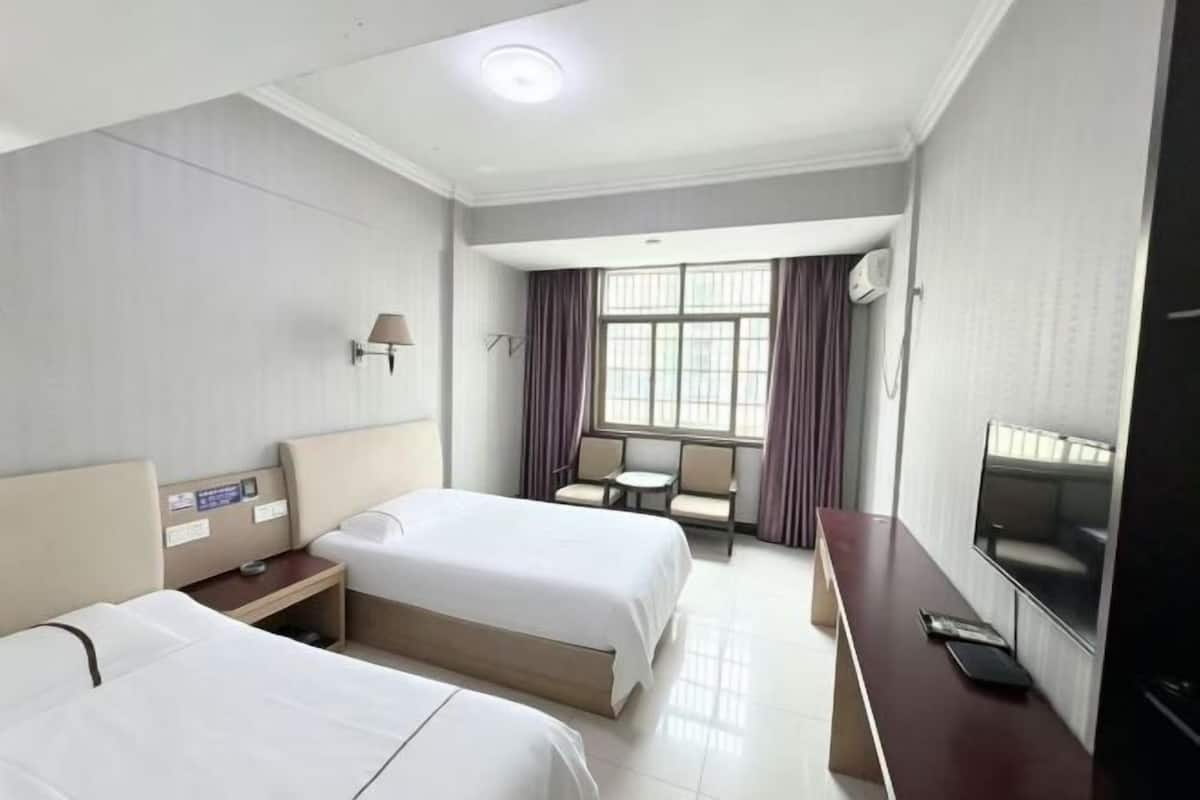 A hotel room with two beds, a desk, a TV, and a window with curtains.