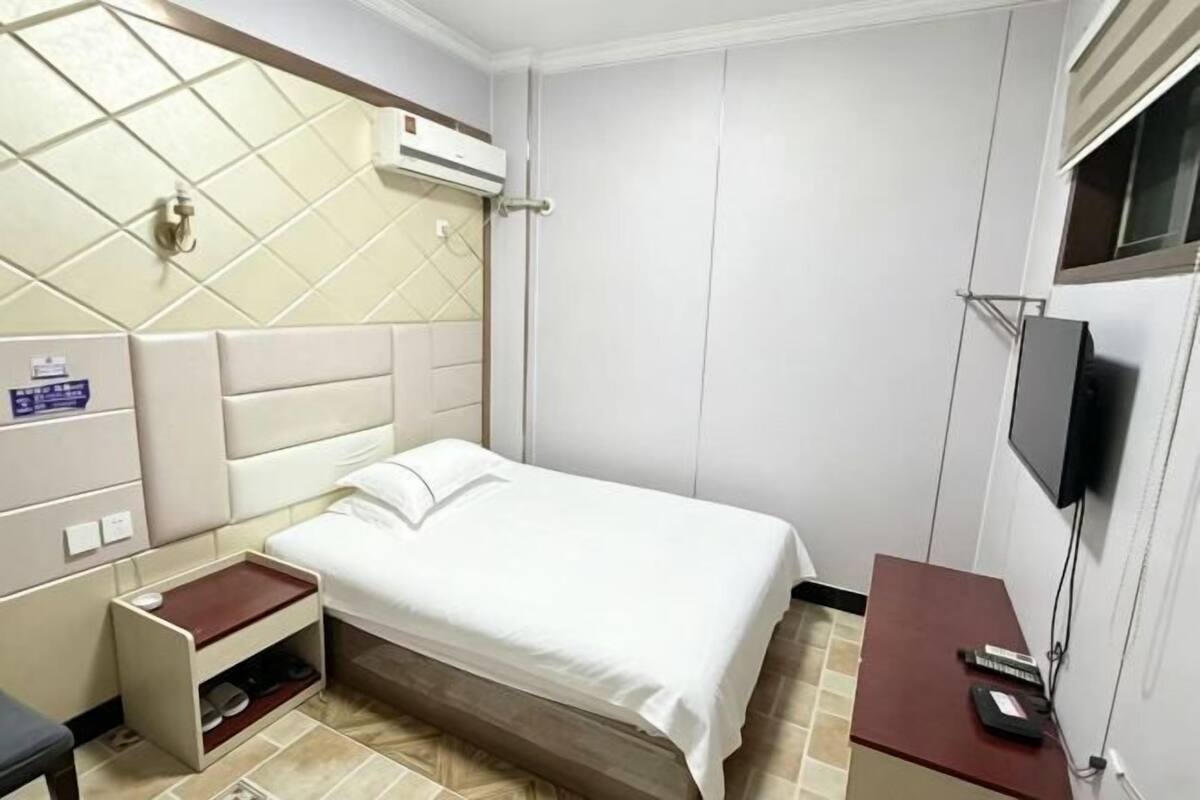 Una habitación de hotel con una cama, televisión, escritorio con computadora y una pequeña estantería.