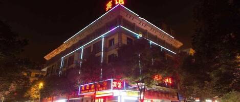 Un hotel con un cartello ben visibile, diversi negozi a livello strada e un furgone parcheggiato davanti.