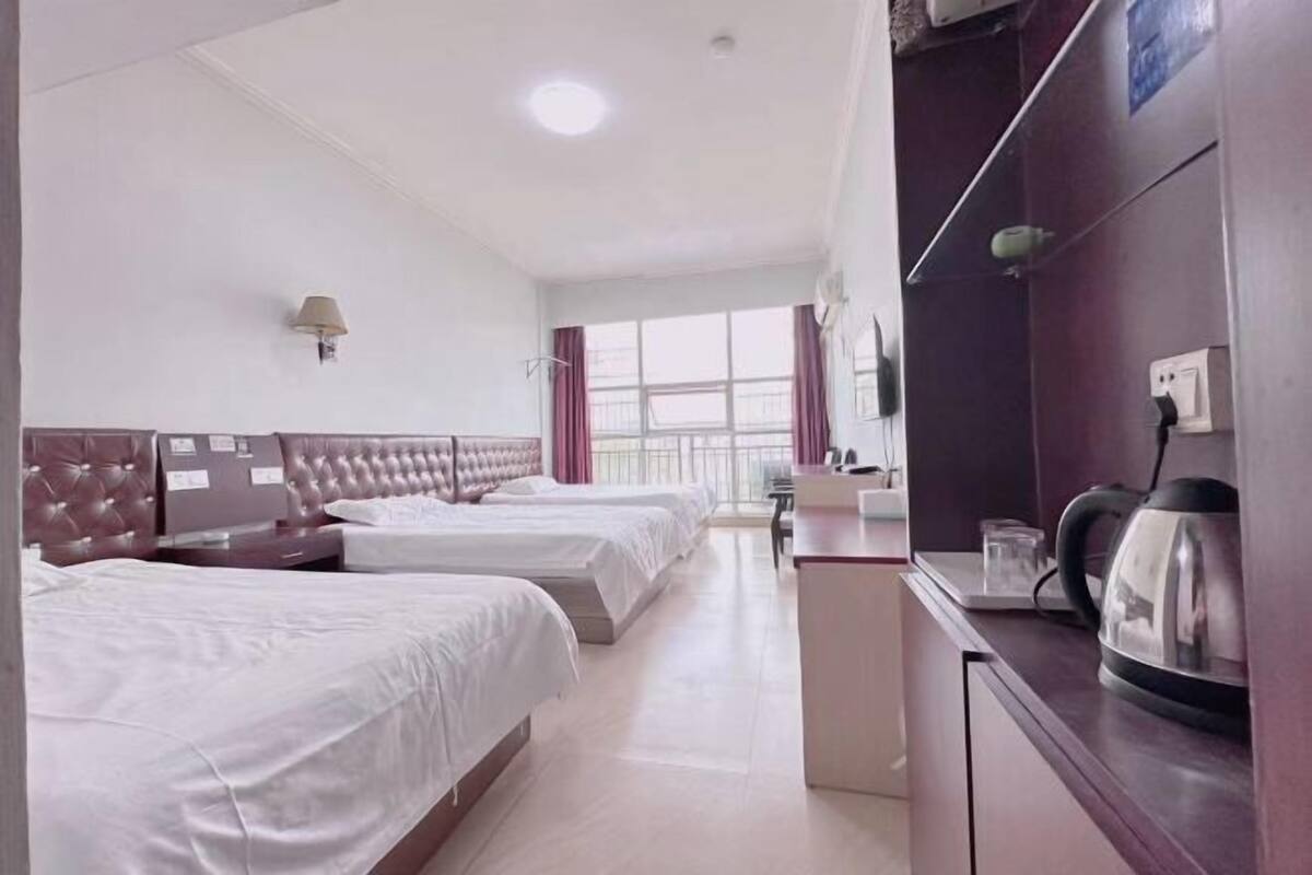 Habitación de hotel con tres camas, un escritorio, una tetera y una ventana con cortinas.