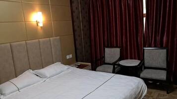 A hotel room with a bed, two chairs, a small table, and a wall-mounted light.