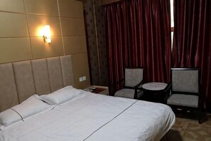 A hotel room with a bed, two chairs, a small table, and a wall-mounted light. - Chuang Wang Fu Hotel (Yiwu)
