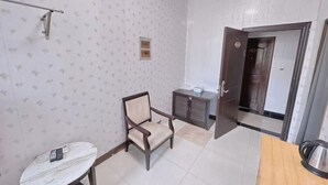 Une pièce avec un papier peint à motifs, une chaise en bois, une petite table, un meuble et une porte donnant sur une autre pièce.