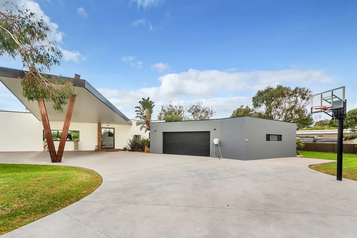 A modern house with a garage, a basketball hoop, and a well-maintained lawn.