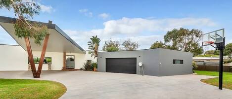 A modern house with a garage, a basketball hoop, and a well-maintained lawn.