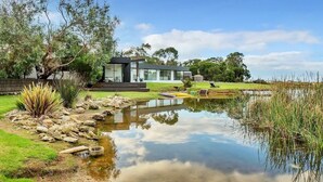 Une maison moderne avec une façade en verre, un étang et une pelouse verdoyante.