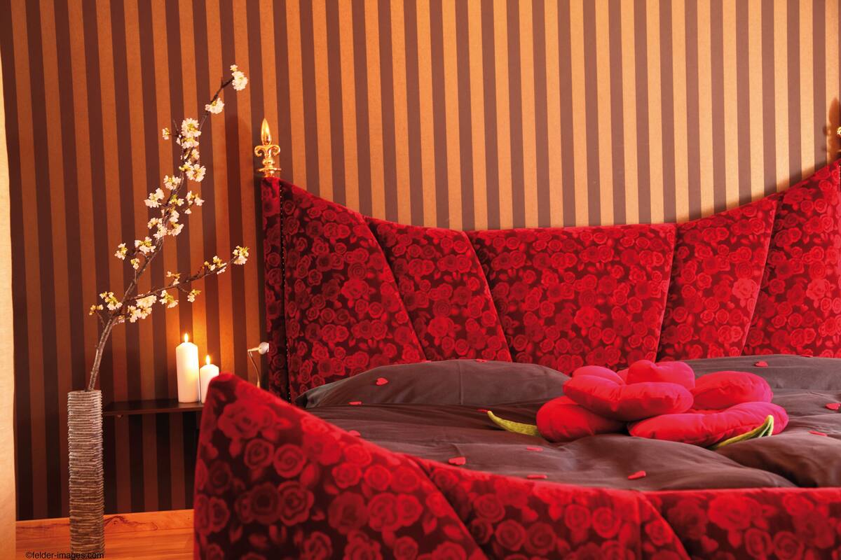 A bedroom with a bed, pillows, a vase with flowers, and a candle on a nightstand.