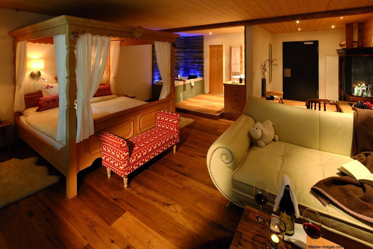 A cozy room with a four-poster bed, a sofa, and a small table with wine glasses.