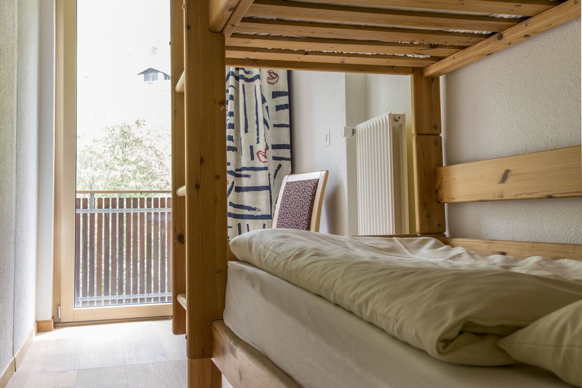 A wooden bunk bed with a view to a balcony.