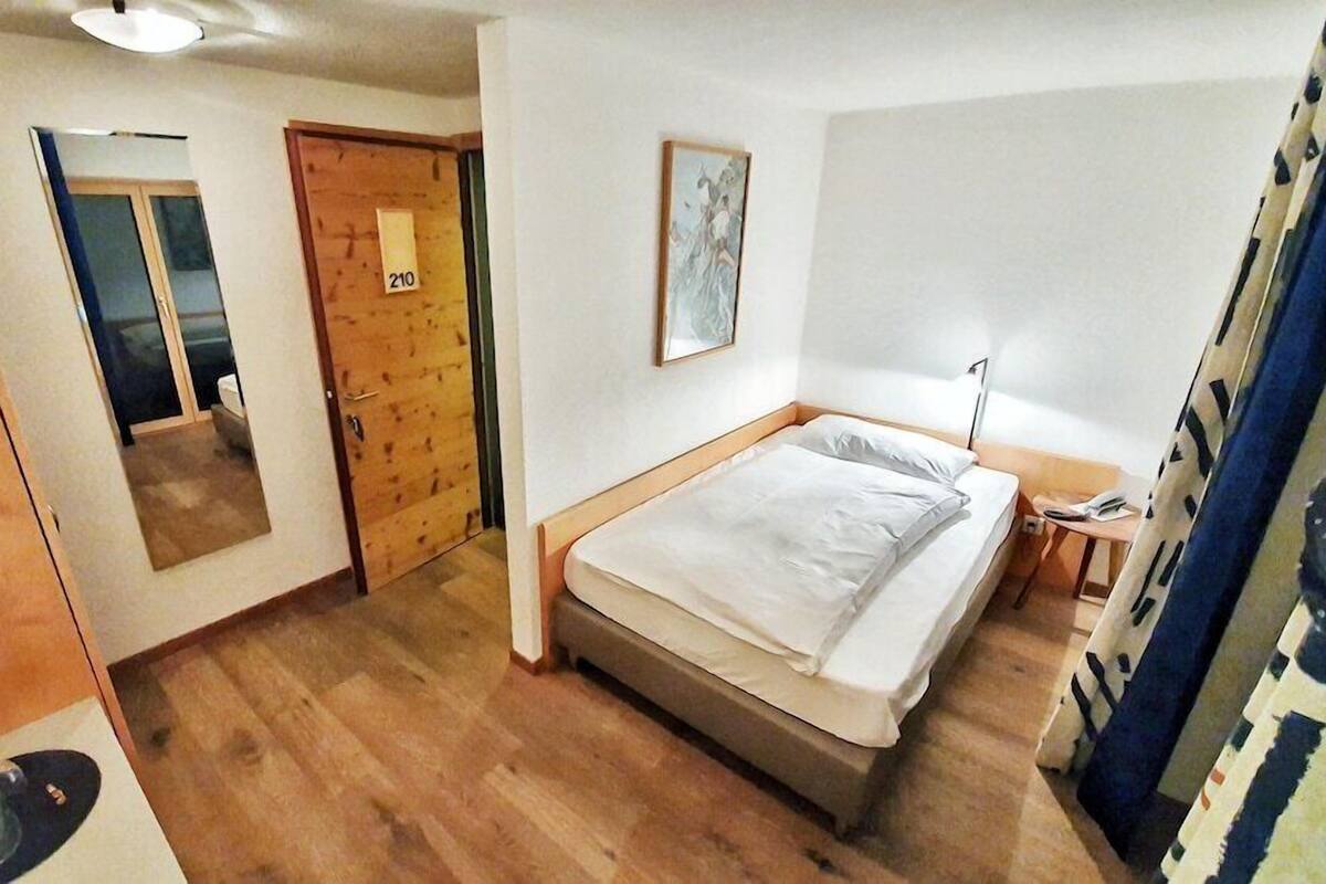 A bedroom with a bed, a wooden door, a mirror, and a painting on the wall.