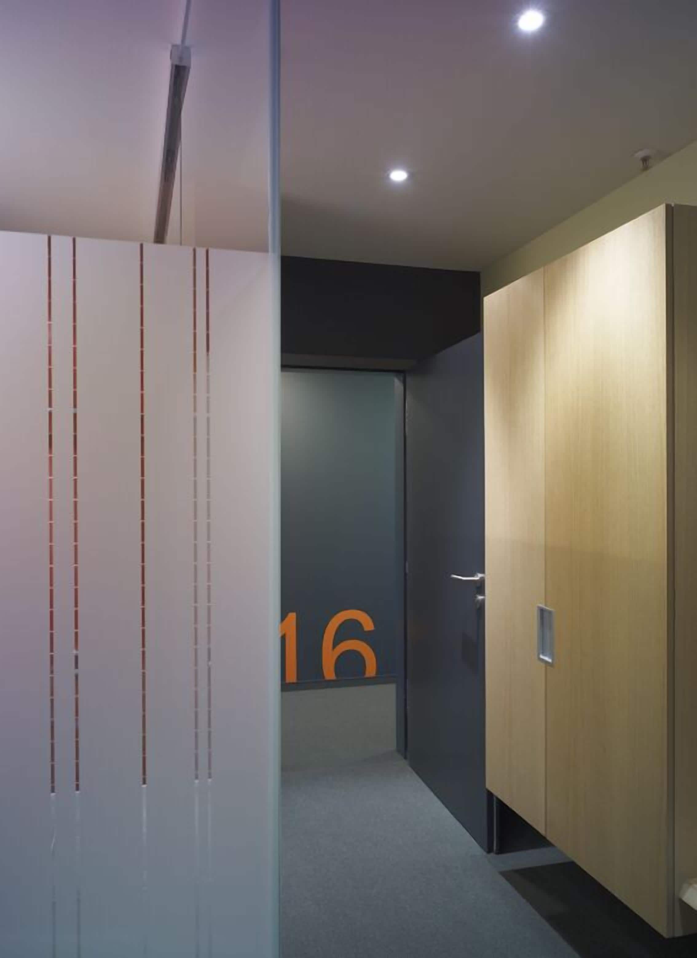 Un pasillo de diseño moderno, con un separador de vidrio con líneas verticales, una puerta con el número 16 y un armario de madera.