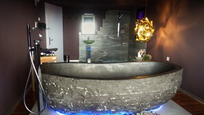 Una bañera de piedra grande y moderna con ducha integrada, iluminada por luces LED azules, en un ambiente de baño contemporáneo.