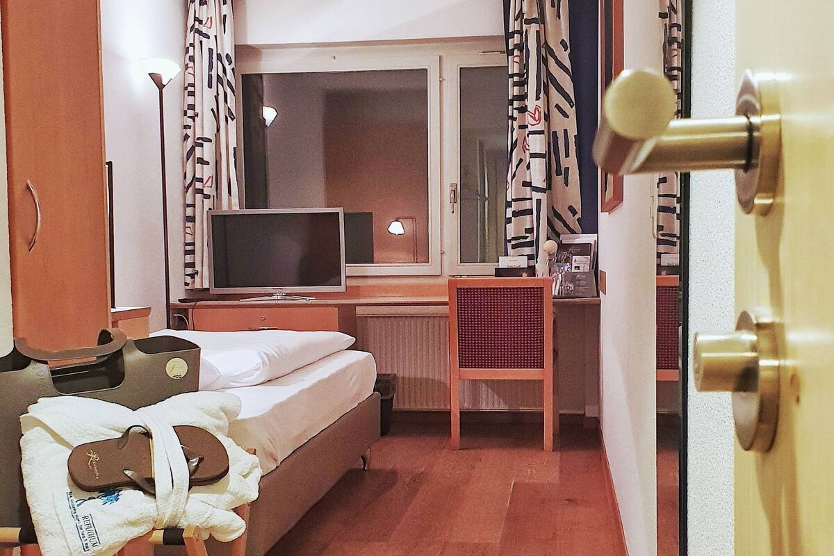A hotel room with a bed, a desk, a chair, a television, and a wardrobe.