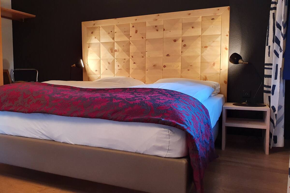A modern bedroom with a wooden headboard, a bed with white linens, and a patterned throw blanket.