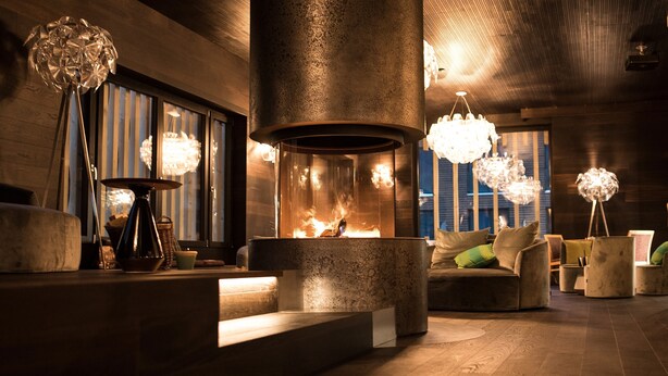 Un área de descanso moderna con una chimenea central, asientos cómodos e iluminación decorativa.