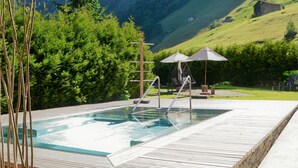 Zona de hidromasaje al aire libre con terraza de madera, una escalera y una silla colgante.