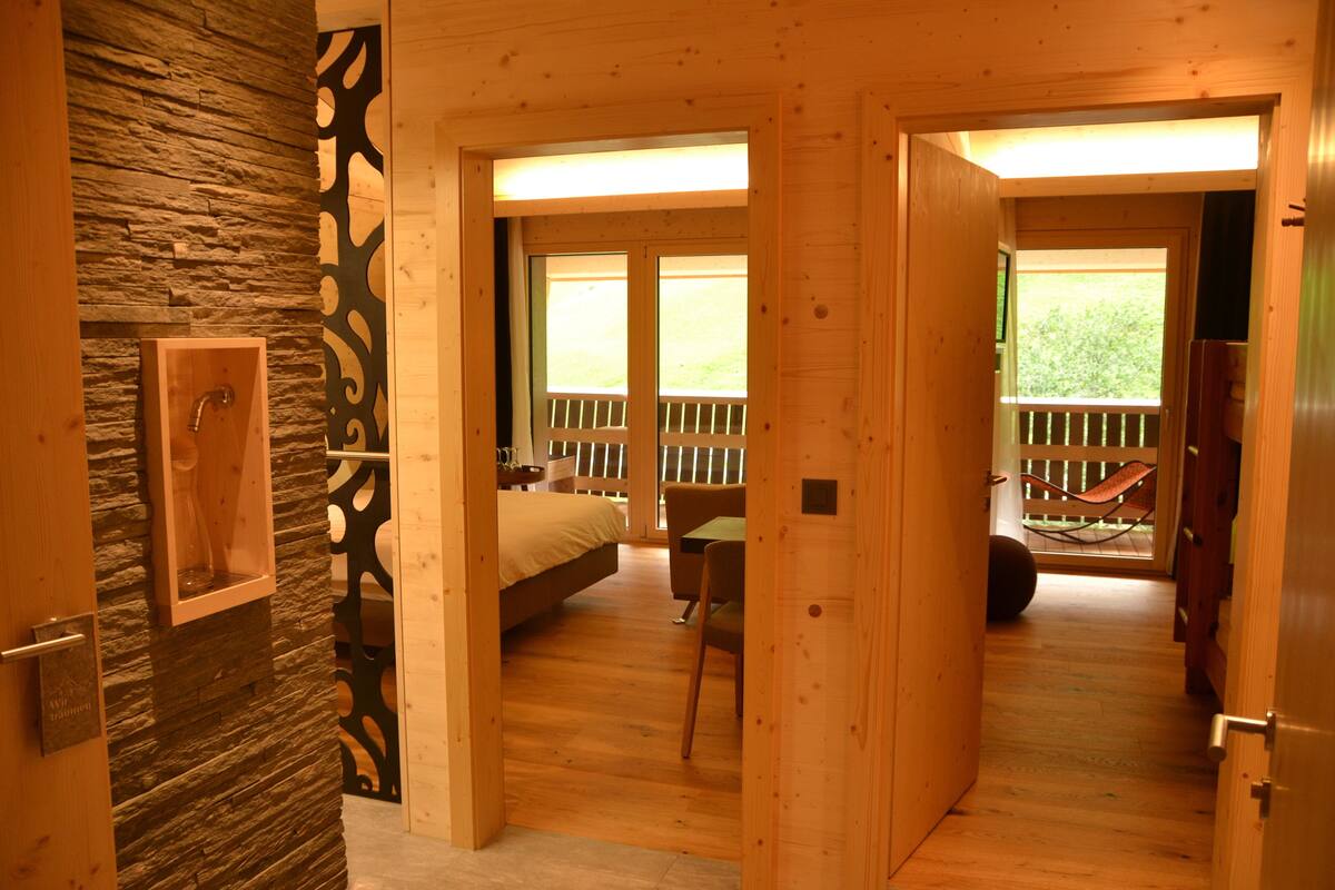 A wooden interior with a stone accent wall, a bed, a dining area, and a balcony with a view.