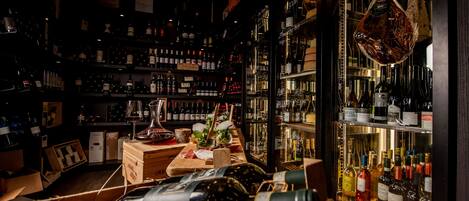 A dimly lit bar with shelves of various bottles, a wooden counter with glasses, and a hanging meat display.
