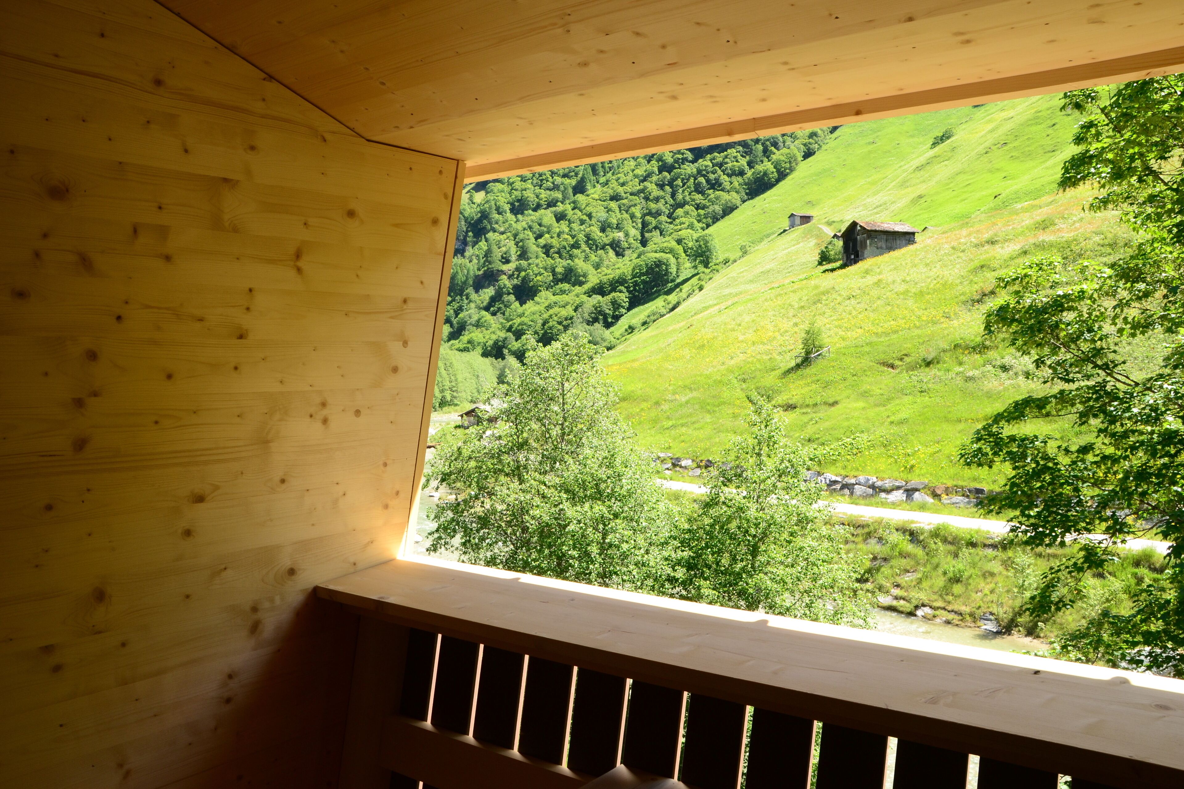 Una cabaña de madera con vistas a una ladera verde y un edificio pequeño a lo lejos.