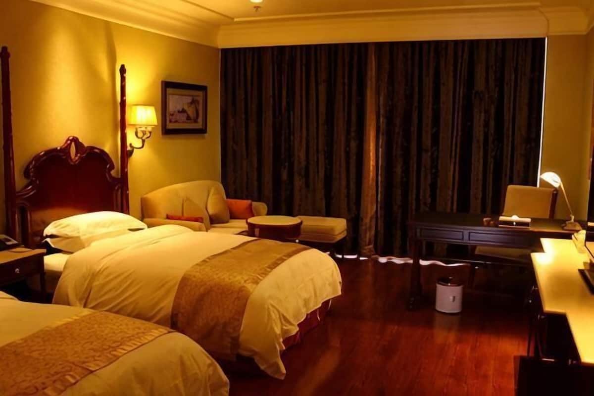 A hotel room with two beds, a desk, a chair, and a piano.