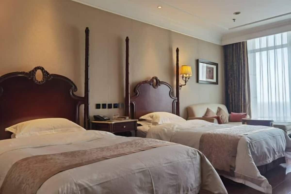 A hotel room with two beds, a nightstand, a lamp, a framed picture, and a window with curtains.