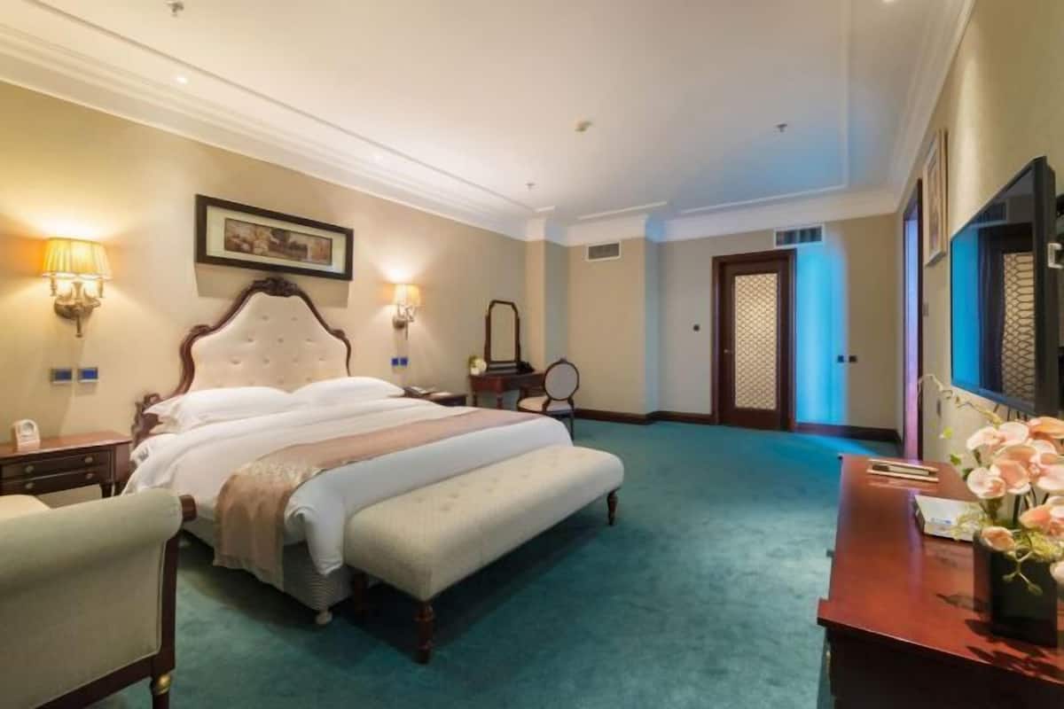 A hotel room with a large bed, bedside lamps, a desk with a vase of flowers, and a mirror.