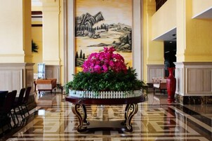 Un vestíbulo con un cuadro grande en la pared, una mesa redonda con un arreglo floral y un jarrón rojo.