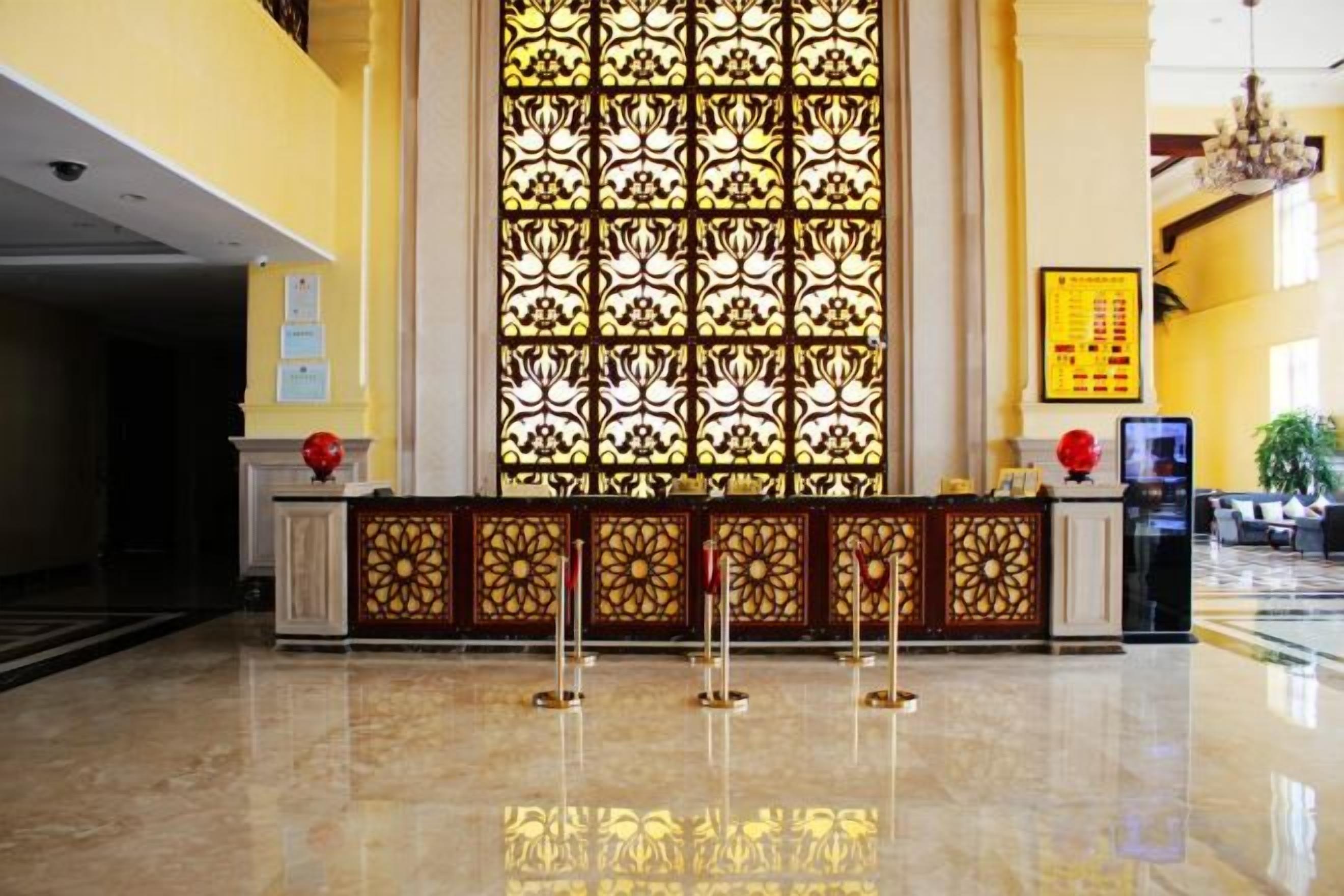A hotel lobby with a reception desk, a large decorative window, and a chandelier.