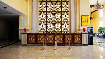 A hotel lobby with a reception desk, a large decorative window, and a chandelier.