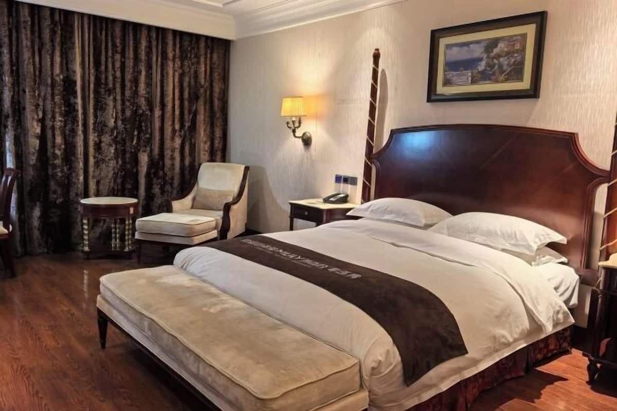 A hotel room with a large bed, a chair, a bedside table, a lamp, and a painting on the wall.