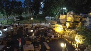 Een buitenterras met houten tafels en banken, omgeven door een rotsachtig landschap met een waterval.
