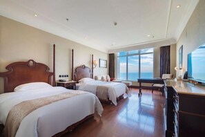 A hotel room with two beds, a desk, a chair, a nightstand, and a large window with a view.