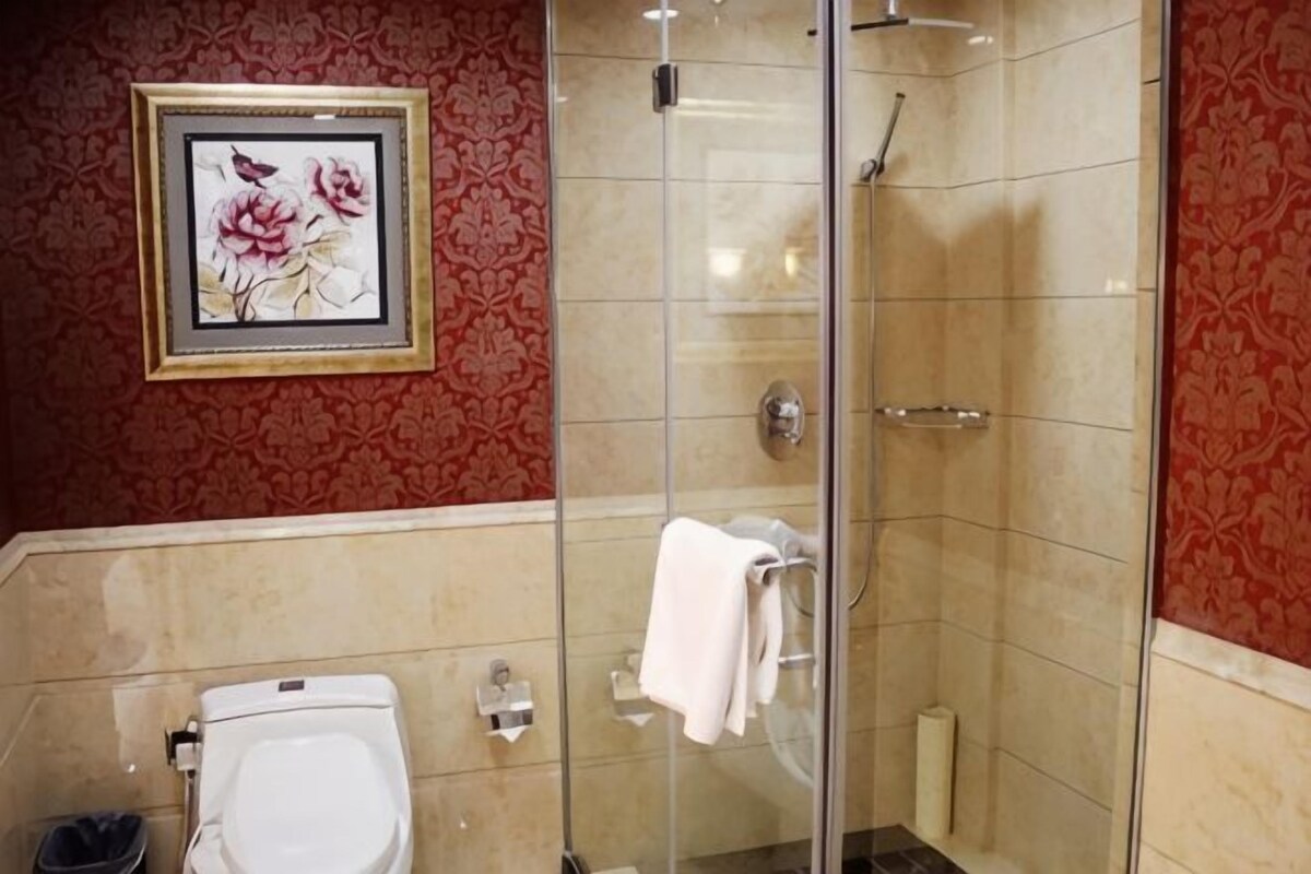 A bathroom with a toilet, a shower enclosure, and a framed floral artwork on the wall.
