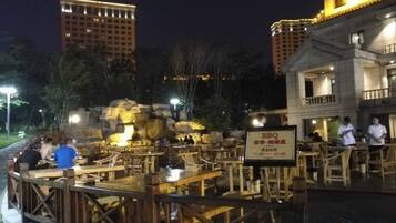 An outdoor dining area with wooden tables and chairs, a rock formation centerpiece, and a sign indicating a BBQ restaurant.
