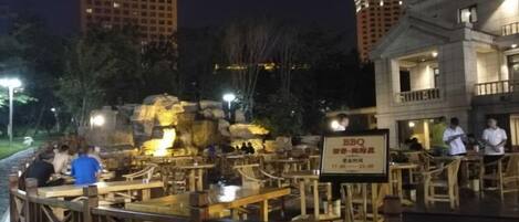 An outdoor dining area with wooden tables and chairs, a rock formation centerpiece, and a sign indicating a BBQ restaurant.