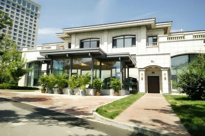 A modern building with a covered entrance, large windows, and a well-maintained lawn.