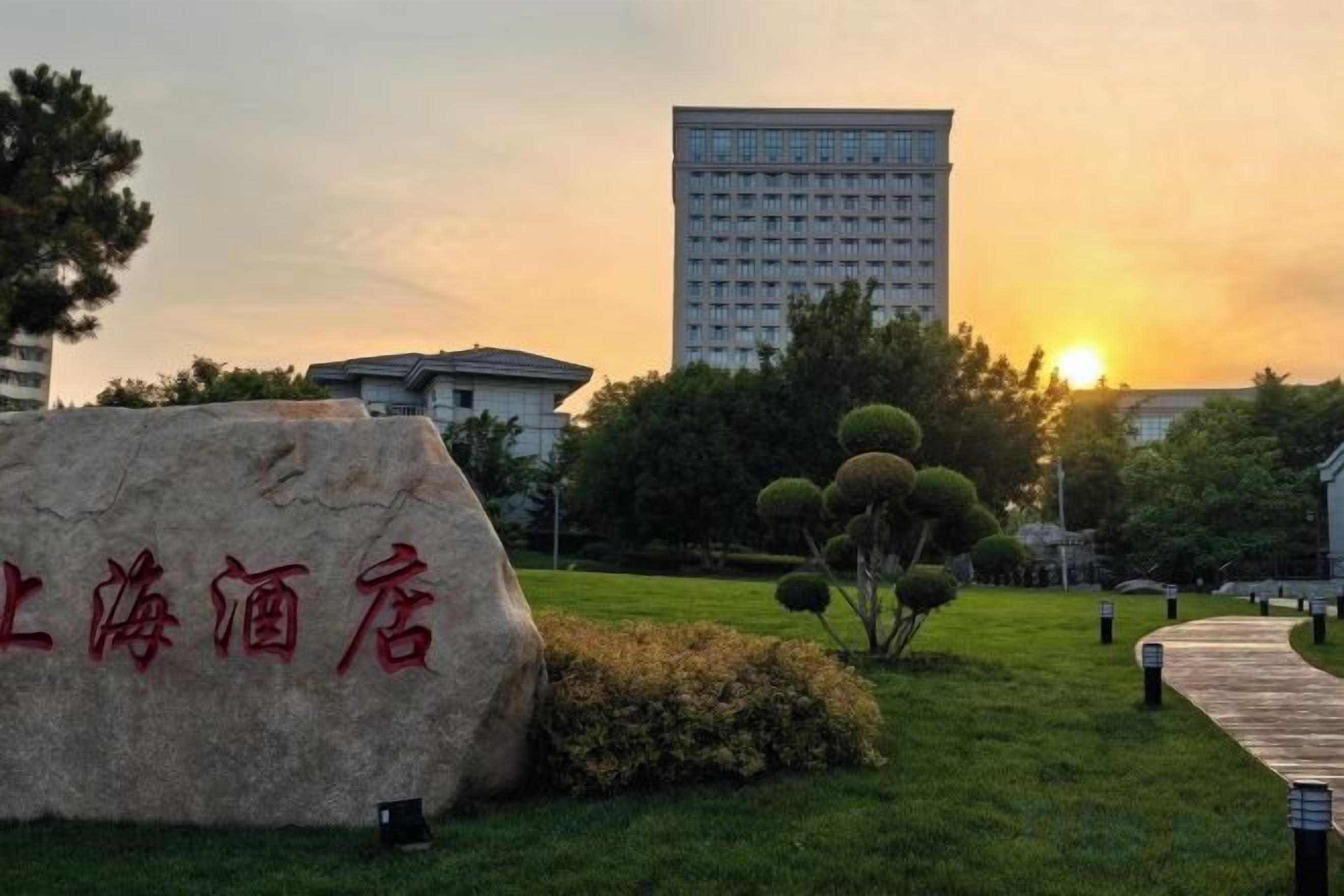 A hotel sign with Chinese characters, a grassy area with a pathway, and a building in the background during sunset.