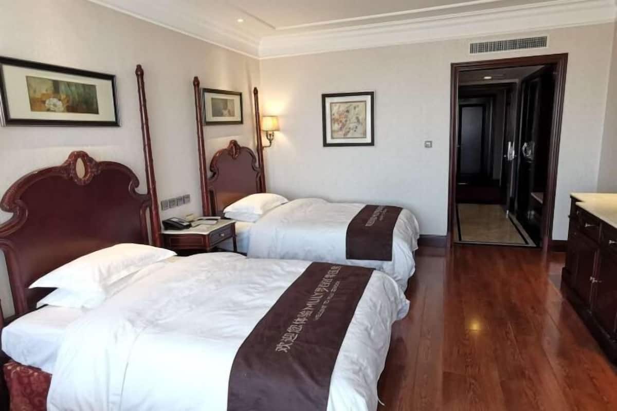 A hotel room with two beds, a wooden headboard, a nightstand, a lamp, and a mirror.