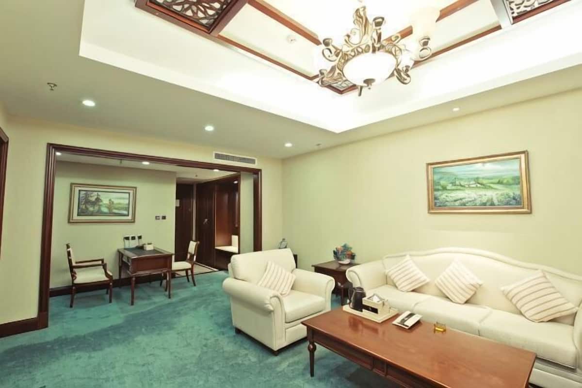 A room with a sofa, armchairs, a coffee table, a painting, and a chandelier.