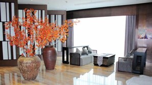 Een moderne woonkamer met een grote vaas oranje bloemen, een zithoek en een groot raam.
