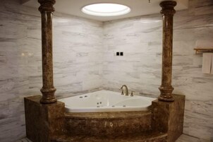Un baño con pared de mármol, una bañera independiente y una lámpara en el techo.