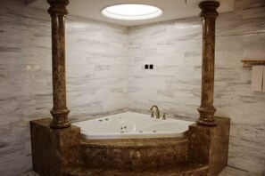 A bathroom with a marble wall, a freestanding bathtub, and a ceiling light.