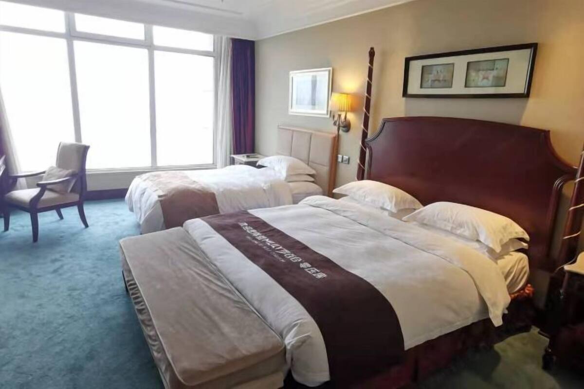 A hotel room with two beds, a chair, a desk, and a large window.