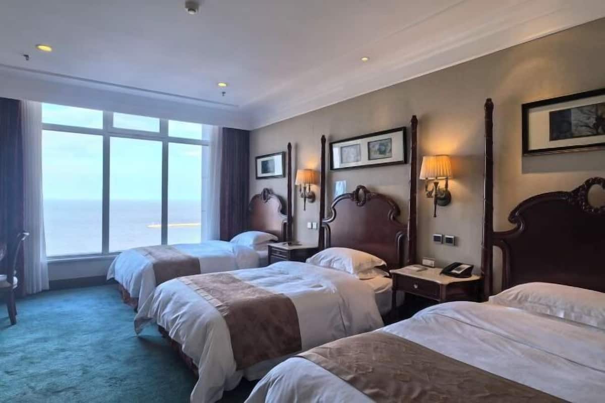 A hotel room with two beds, a large window, and a view of the sea.