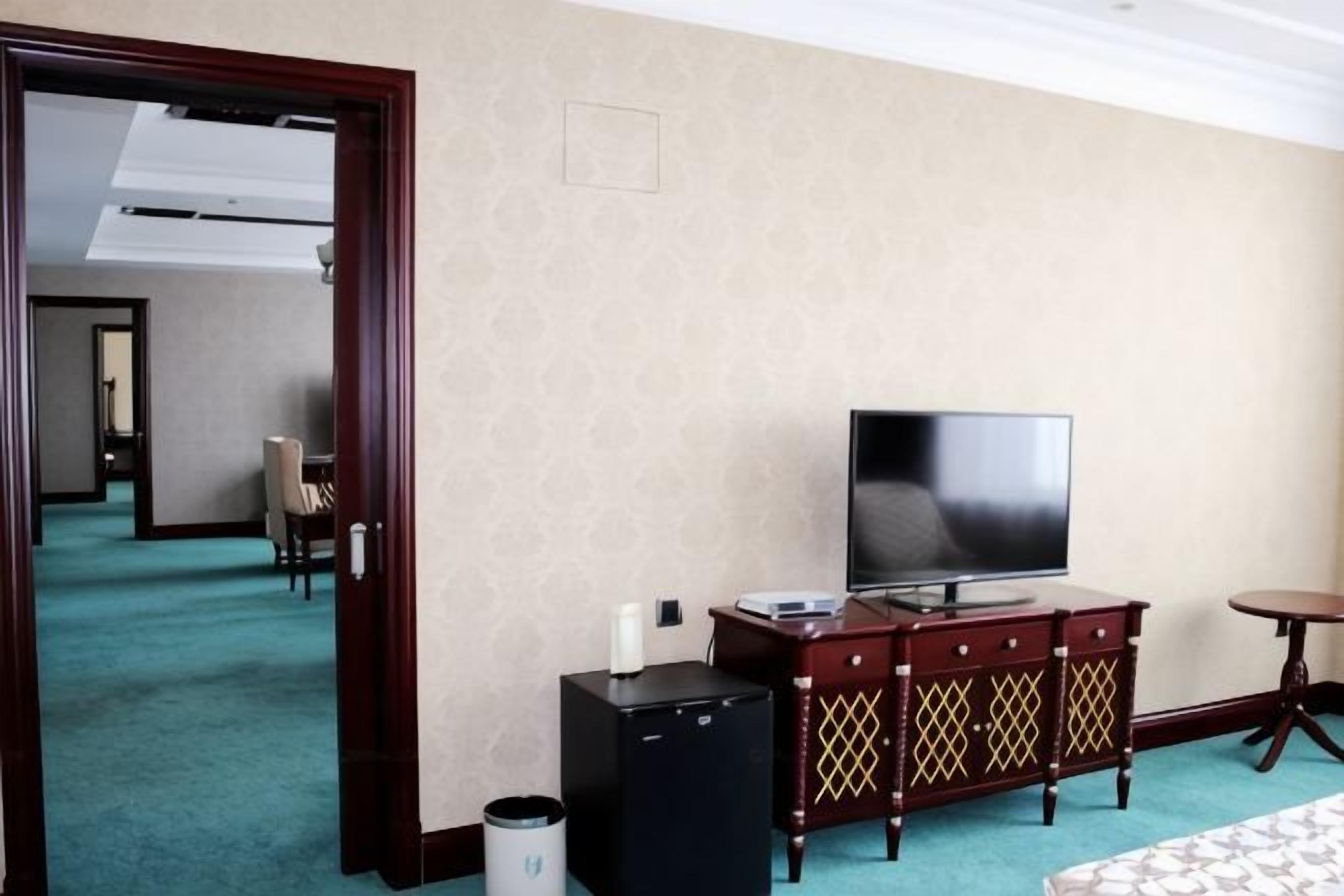 A hotel room with a television, a minibar, and a small table.