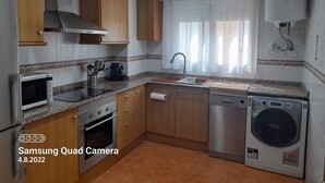 Een moderne keuken met houten kastjes, een RVS-fornuis, een magnetron, een spoelbak en een wasmachine.
